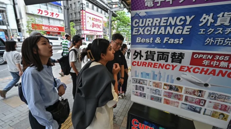 Người dân đứng bên ngoài quầy đổi tiền để xem tỷ giá đồng yên so với ngoại tệ, dọc con phố ở trung tâm Tokyo vào ngày 29/4/2024. Ảnh: AFP