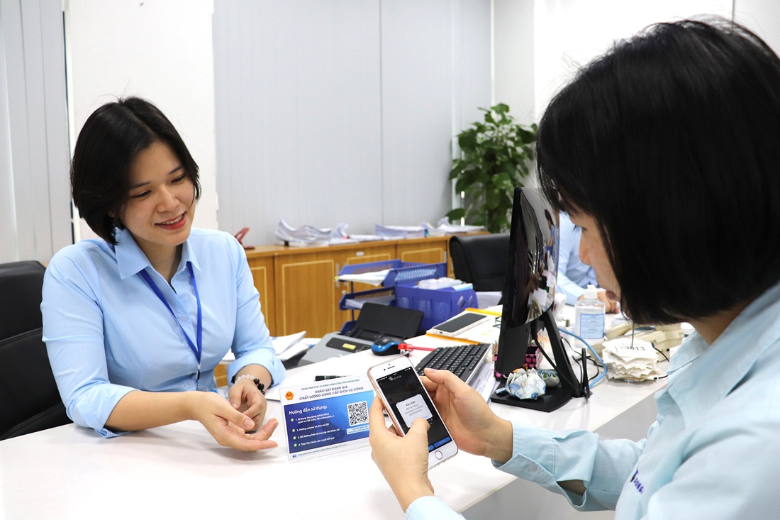 Cán bộ Trung tâm Phục vụ hành chính công tỉnh hướng dẫn người dân đánh giá sự hài lòng qua việc quét mã QR. Ảnh: Báo Quảng Ninh