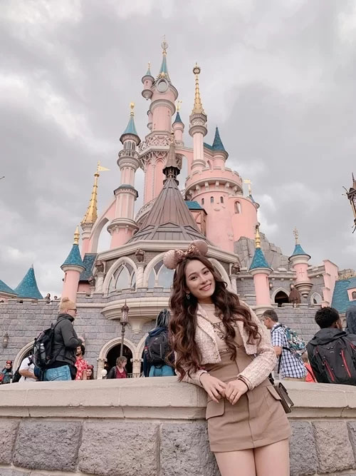 Nữ ca sĩ tạo dáng bên lâu đài cổ tích trong công viên Disneyland.