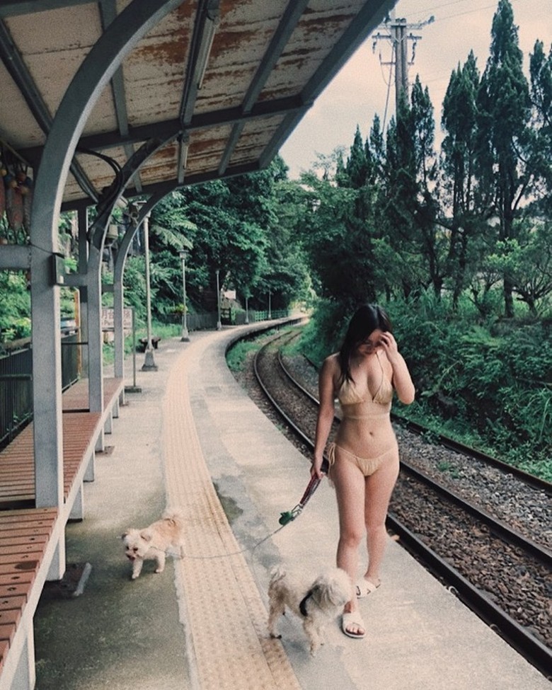 Nữ ca sĩ mặc một bộ đồ tắm hai mảnh màu vàng nhạt, đưa hai chú chó đi dạo ở nhà ga trông rất thoải mái.
