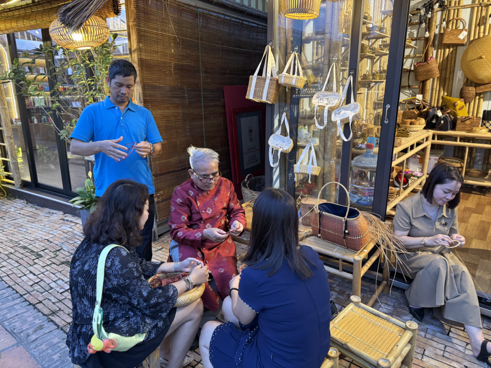 Nghệ nh&acirc;n nh&acirc;n d&acirc;n l&agrave;ng m&acirc;y tre đan Ph&uacute; Vinh hướng dẫn du kh&aacute;ch l&agrave;m v&ograve;ng tay m&acirc;y tre đan tại Hồ Văn. Ảnh: Hồ Hạ.