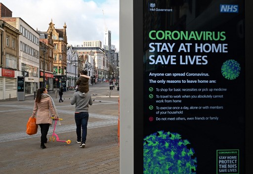 Người đi ngang qua một bảng điện tử hiển thị khuyến cáo phòng chống dịch Covid-19 của chính phủ Anh tại một trung tâm mua sắm ở thành phố Leeds. Ảnh: AFP