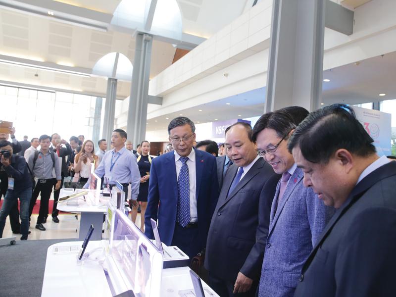 Thủ tướng Chính phủ Nguyễn Xuân Phúc (thứ ba, từ phải qua), Bộ trưởng Bộ Kế hoạch và Đầu tư Nguyễn Chí Dũng (ngoài cùng, bên phải) thăm gian hàng của Sam sung tại triển lãm tổ chức nhân Hội nghị 30 năm thu hút FDI