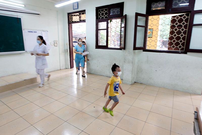 Một bé trai chạy ào ra khỏi vòng tay mẹ khi chuẩn bị tới lượt lấy mẫu xét nghiệm.